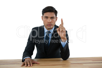 Portrait of confident businessman pointing upwards while sitting at table