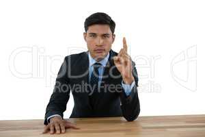 Portrait of confident businessman pointing upwards while sitting at table