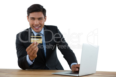 Portrait of businessman holding credit card while using laptop