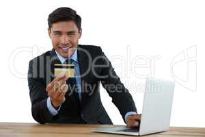 Portrait of businessman holding credit card while using laptop