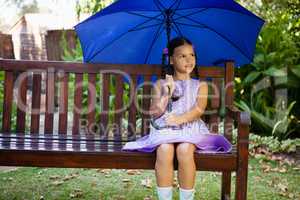 Girl sitting with blue umbrella on wooden bench