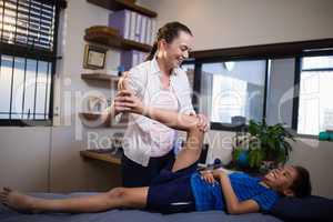 Smiling female therapist massaging leg of boy lying on bed