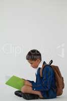 Schoolboy reading book against white background