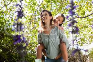 Low angle view of smiling woman giving daughter piggyback ride against trees