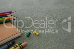Color pencils, crayons, push pins and book on chalkboard