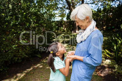 Side view of smiling grandmother and granddaughter standing while holding hands