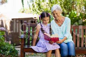 Smiling grandmother reading book to granddaughter while sitting on wooden bench