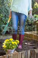 Low section of senior woman holding garden fork and potted plant