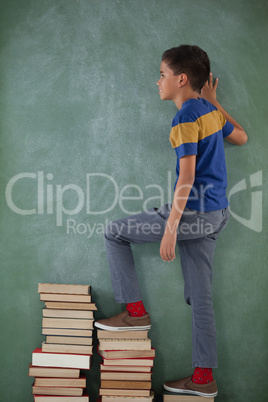 Schoolboy climbing steps of books stack