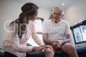 Low angle view of female therapist pointing at knee while male patient sitting on bed