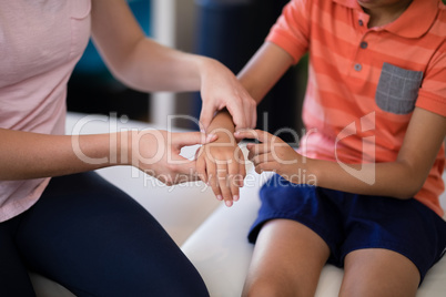 Midsection of female therapist examining hand with boy sitting on bed