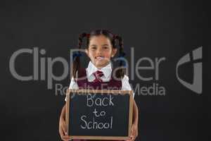 Portrait of schoolgirl holding slate with text against blackboard