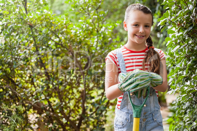 Portrait of smiling girl standing with gardening fork against plants