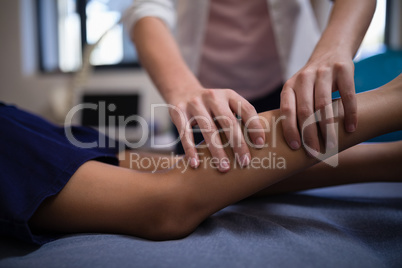Midsection of female therapist massaging calf with boy lying on bed