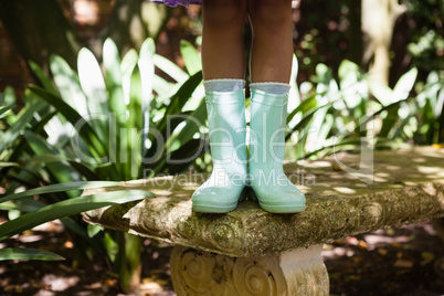 Low section of girl wearing green rubber boot standing on stone bench