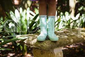 Low section of girl wearing green rubber boot standing on stone bench