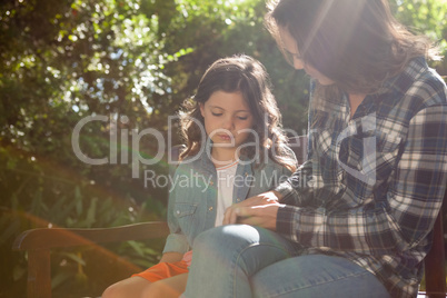 Beautiful mother sitting with girl on bench against plants at backyard