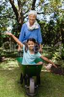 Smiling senior woman pushing wheelbarrow with granddaughter