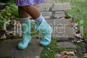 Low section of girl wearing green rubber boots standing on walkway