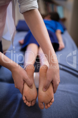 Boy lying on bed while receiving foot massage from young female therapist