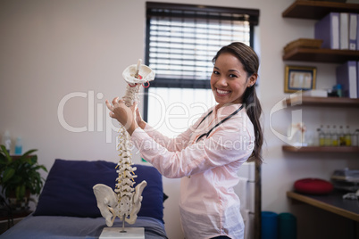 Portrait of smiling female therapist examining artificial spine on bed