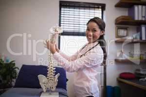Portrait of smiling female therapist examining artificial spine on bed