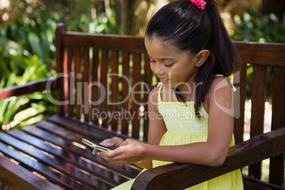 Smiling girl using cellphone while sitting on wooden bench