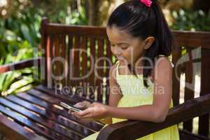 Smiling girl using cellphone while sitting on wooden bench
