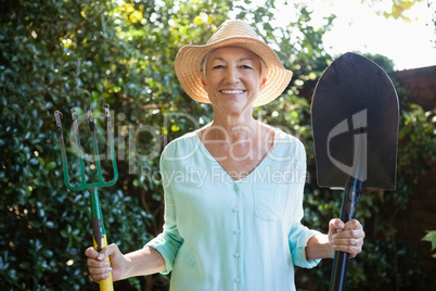 Portrait of smiling senior woman holding garden fork and shovel