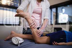 Low section of boy lying on bed while receiving calf massage from female therapist