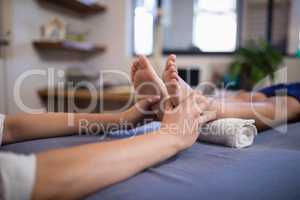 Low section of boy lying on bed while receiving foot massage from female therapist