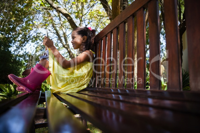Surface level view of smiling girl using mobile phone while sitting on wooden bench