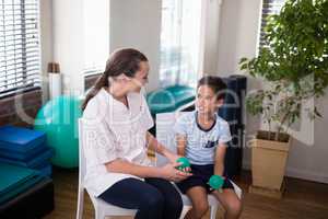 Smiling female therapist looking at boy holding stress balls while sitting on chairs
