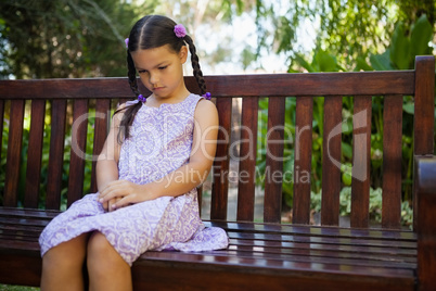 Upset girl looking down while sitting on wooden bench