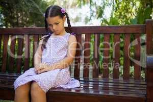 Upset girl looking down while sitting on wooden bench