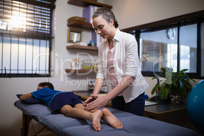 Young female therapist massaging calf of boy lying on bed
