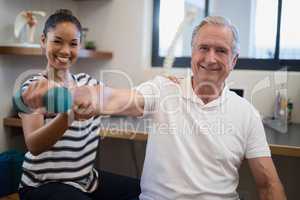 Portrait of smiling female doctor with senior male patient holding dumbbell