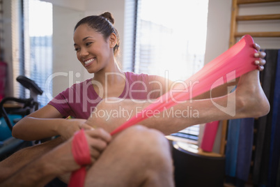 Low section of senior male patient pulling resistance band by smiling female therapist