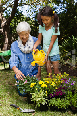 Senior woman looking at girl watering flowers
