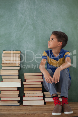 Schoolboy sitting on books stack against chalkboard