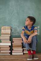Schoolboy sitting on books stack against chalkboard