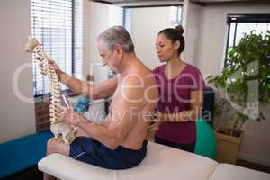 Shirtless male patient holding artificial spine while female therapist examining back