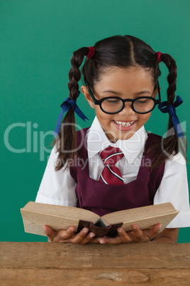 Schoolgirl reading book against chalkboard