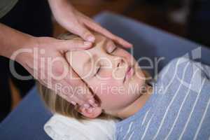 High angle view of boy lying with eyes closed receiving head massage from female therapist