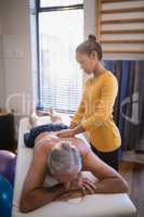 Young female therapist massaging back of senior male patient against window