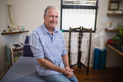 Portrait of smiling senior male patient sitting on bed against window