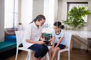 Female therapist showing digital tablet to boy sitting on chairs