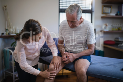 Female therapist examining knee of senior male patient