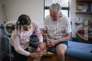 Female therapist examining knee of senior male patient
