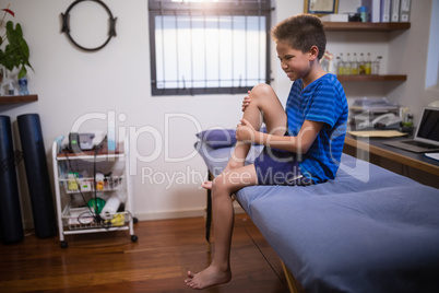 Boy frowning with knee pain while sitting on bed